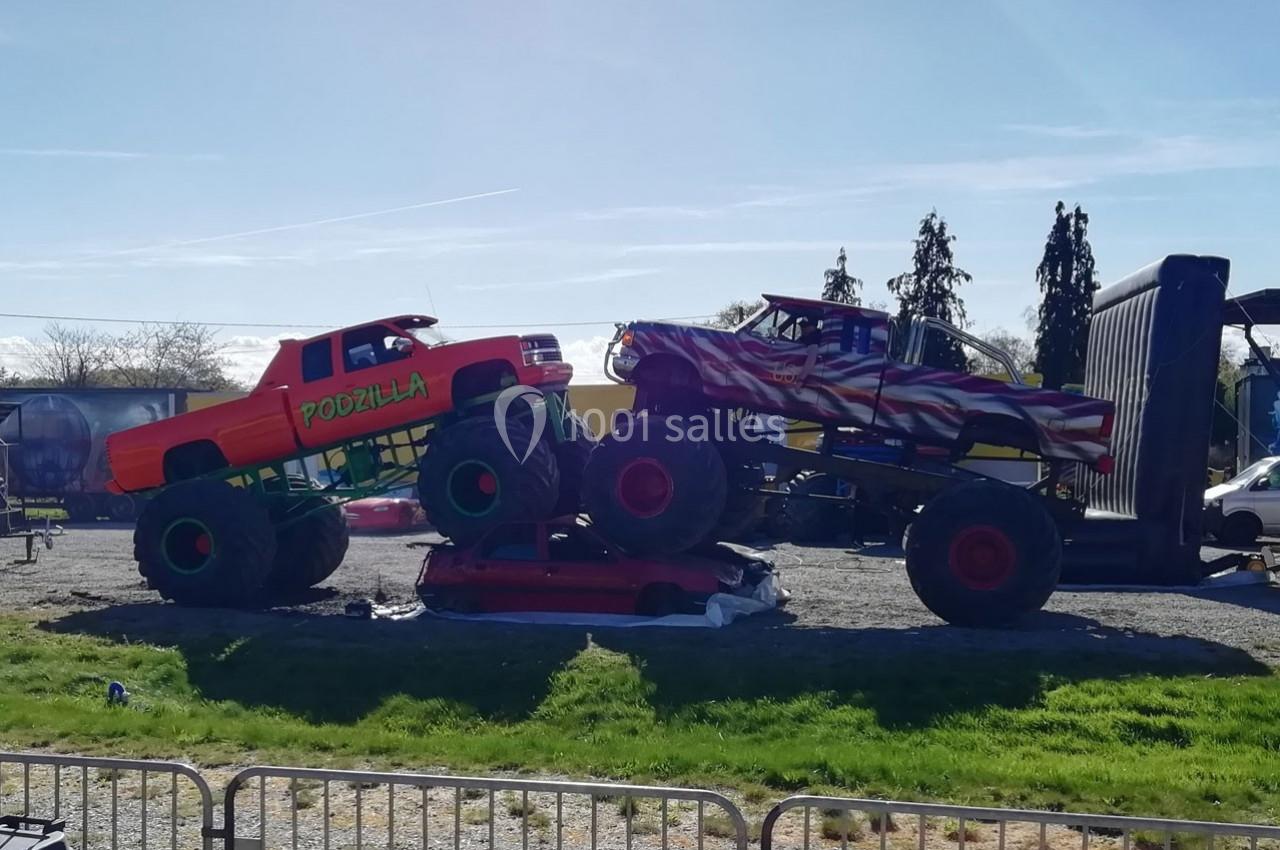 Deux monster trucks en plein spectacle, l'un écrasant une voiture tandis que l'autre est incliné dessus.