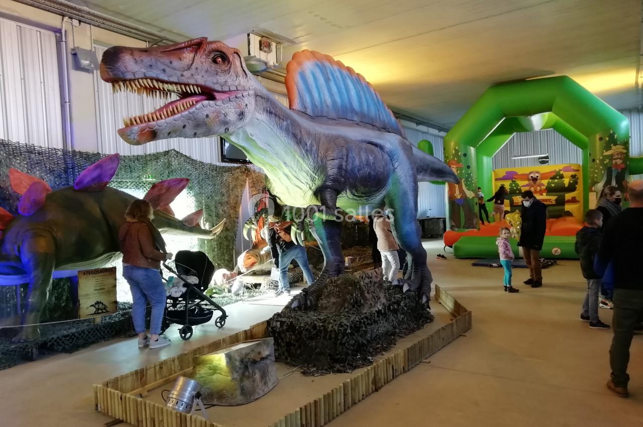 Reconstitution d'un dinosaure à crête dans une exposition intérieure avec des visiteurs et une aire de jeux gonflable.