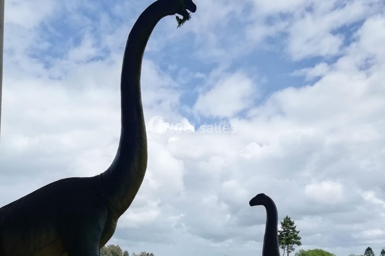 Deux statues de dinosaures au long cou dans un paysage extérieur sous un ciel partiellement nuageux.