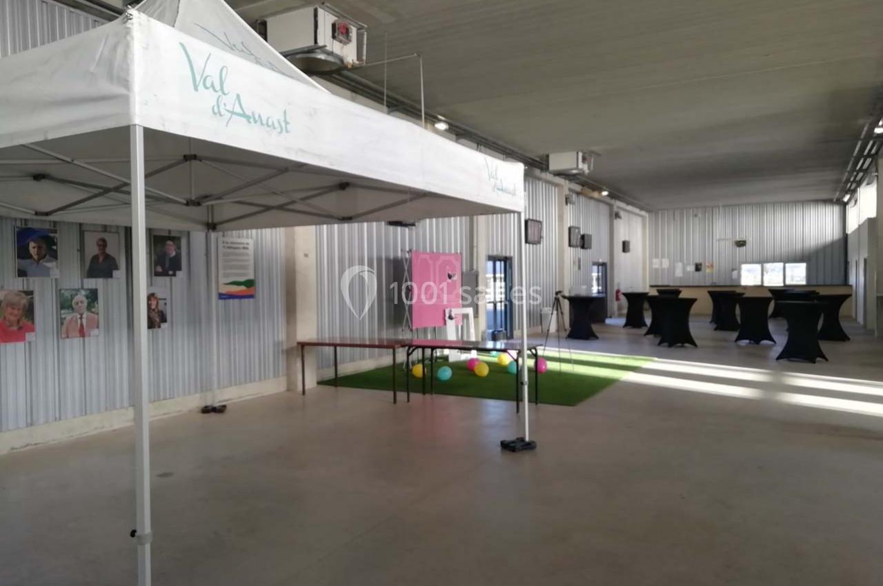 Intérieur d'une salle avec un stand sous une tente blanche, des tables hautes et des décorations colorées.