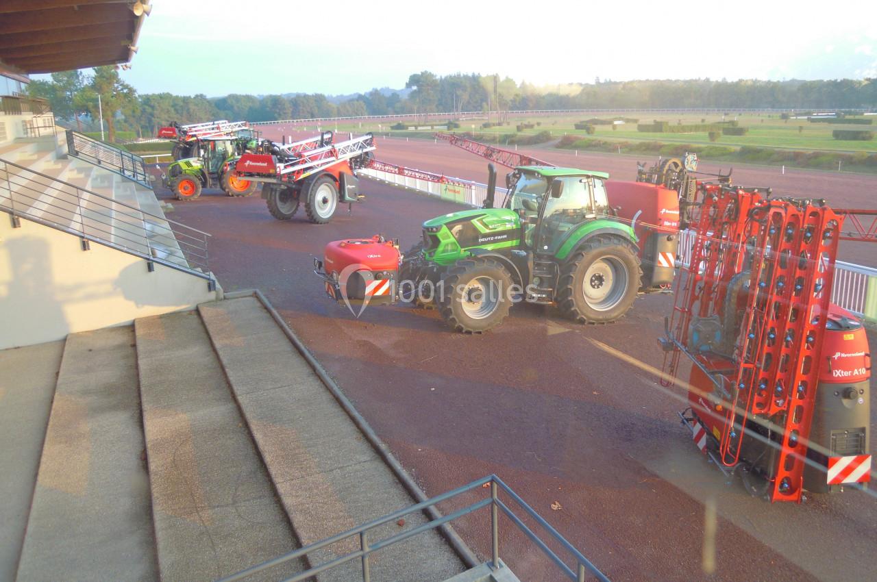 Tracteurs agricoles équipés de pulvérisateurs stationnés sur une piste en plein air, près de gradins.