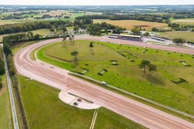 Un motocycliste effectue un saut spectaculaire au-dessus de véhicules dans un espace extérieur ensoleillé.