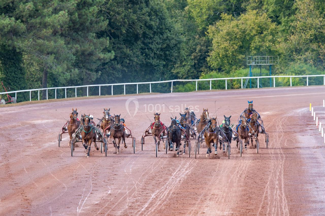 Course de trot attelé avec plusieurs chevaux et conducteurs sur une piste en terre, entourée de végétation.