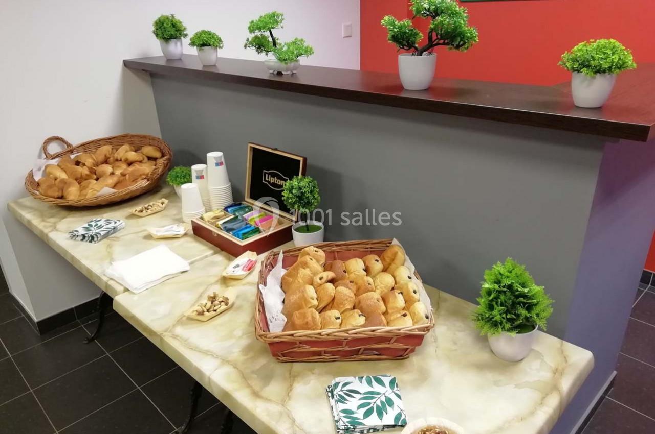 Table avec viennoiseries, noix, serviettes et boissons disposées près d'un comptoir dans un espace intérieur.