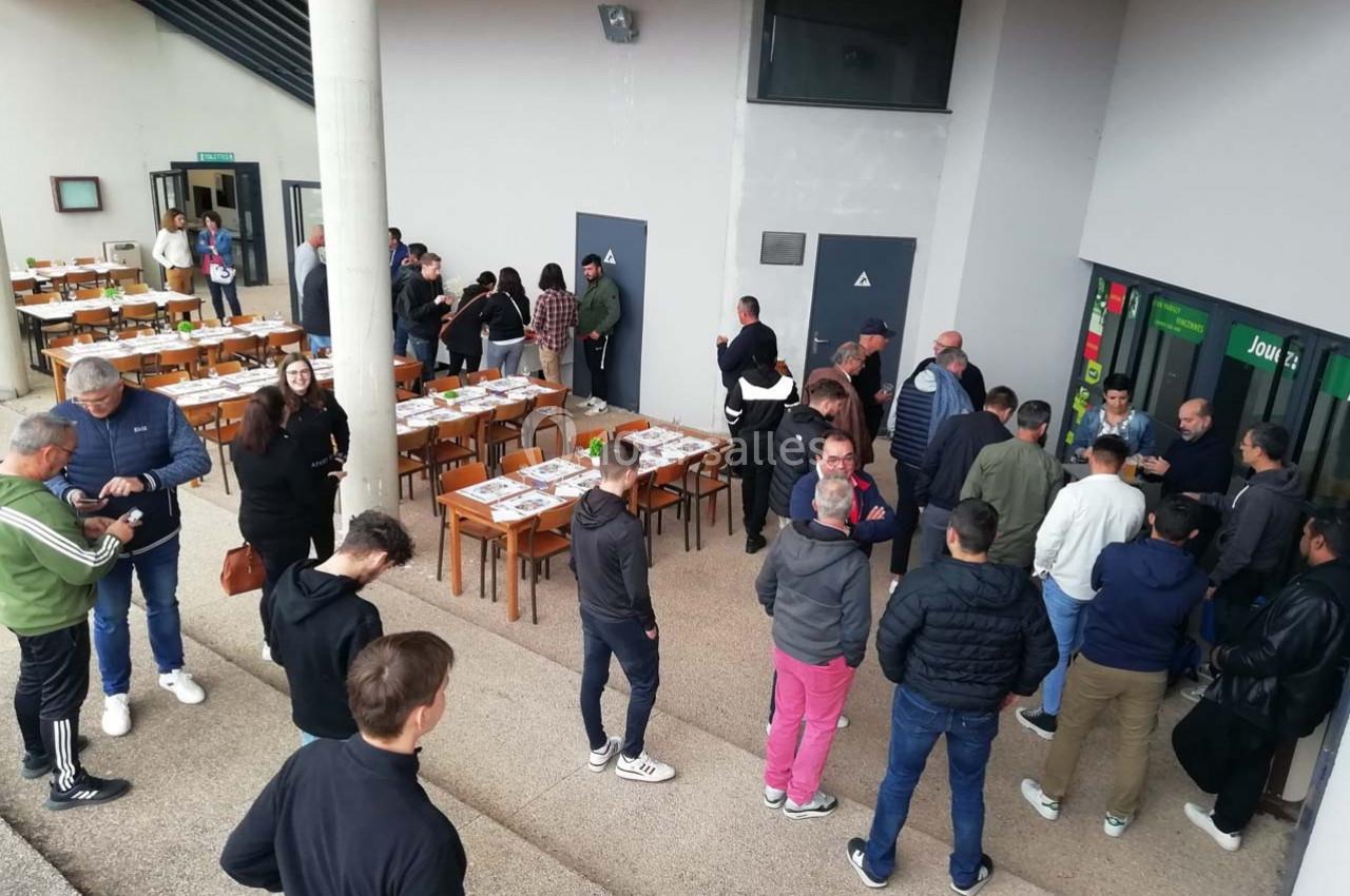 Des personnes rassemblées devant une entrée, près de tables disposées en extérieur, dans un espace semi-ouvert.