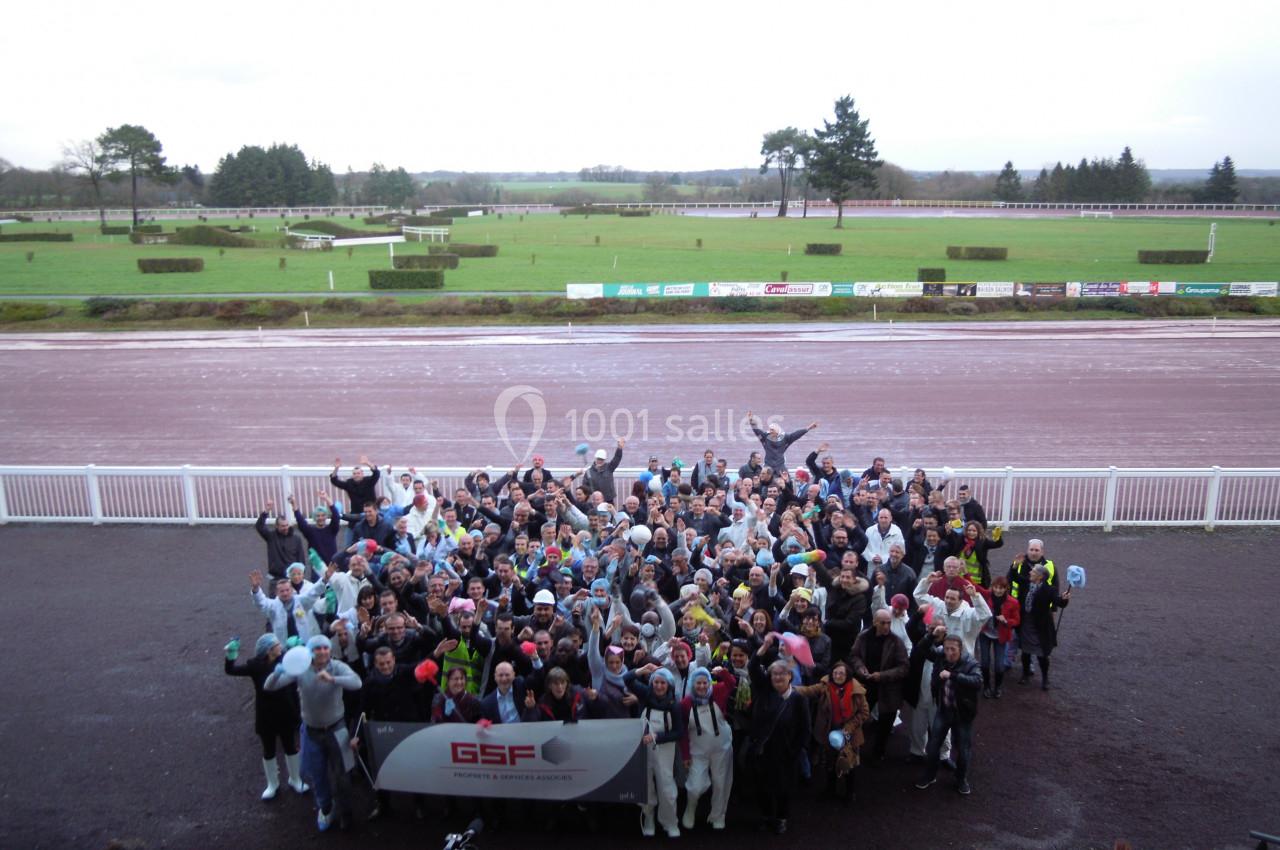 Un groupe de personnes rassemblées en extérieur devant une piste, brandissant une banderole, sur un fond de paysage ouvert.