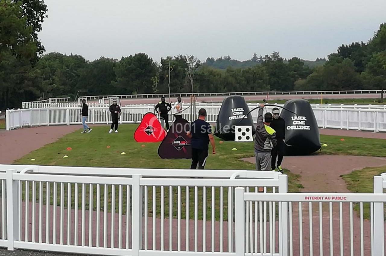 Des personnes participent à une activité de tir sur un terrain herbeux entouré de barrières blanches.