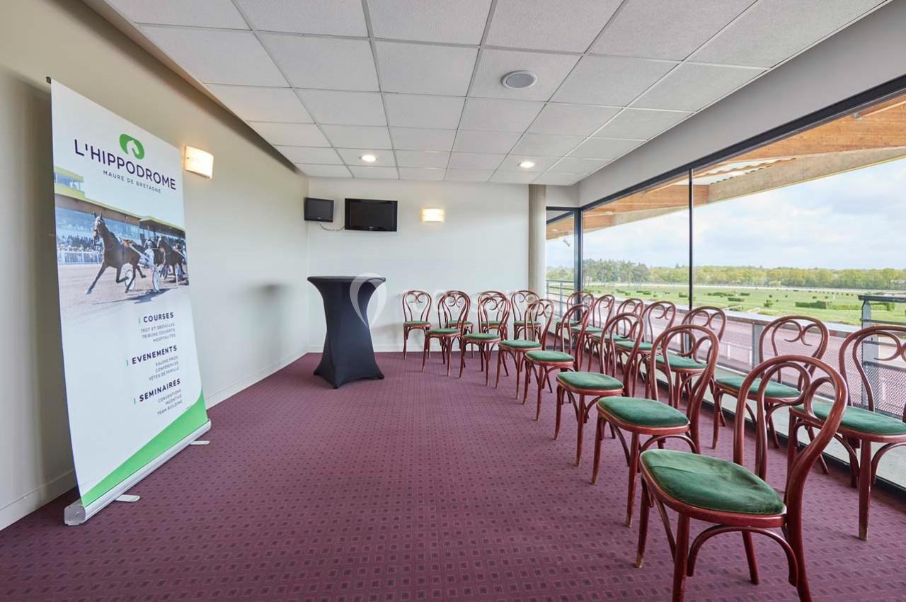 Salle de réunion avec chaises alignées, table haute et vue sur l'extérieur, affichant un panneau promotionnel de l…