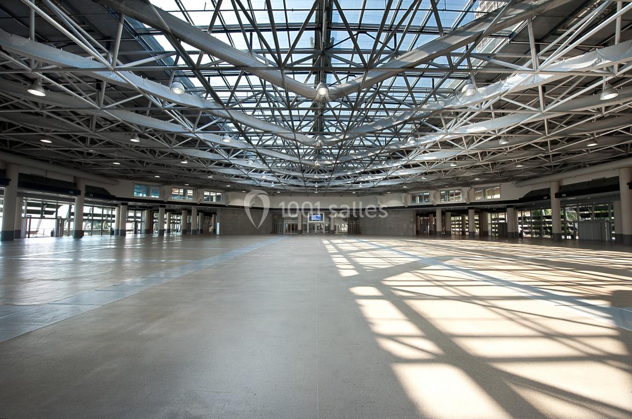 Vue intérieure d'un grand hall vide avec une structure métallique apparente et un plafond en verre laissant entrer la…