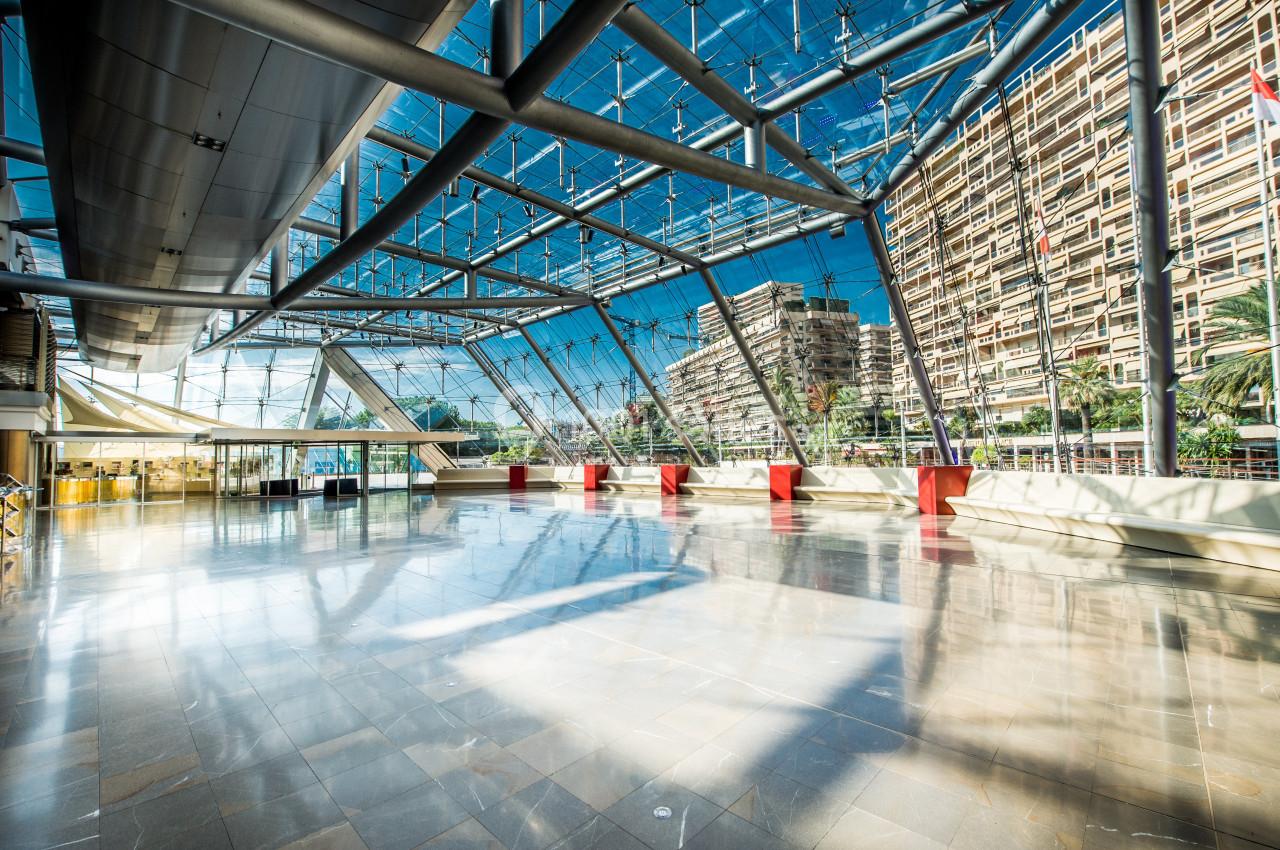 Hall spacieux avec sol en marbre, grandes baies vitrées et vue sur des immeubles modernes et des palmiers.