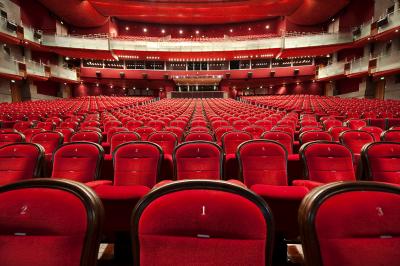 Salle de conférence lumineuse avec des rangées de chaises en bois, deux écrans et de grandes fenêtres donnant sur l…