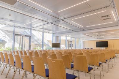 Salle de conférence lumineuse avec des rangées de chaises en bois, deux écrans et de grandes fenêtres donnant sur l…