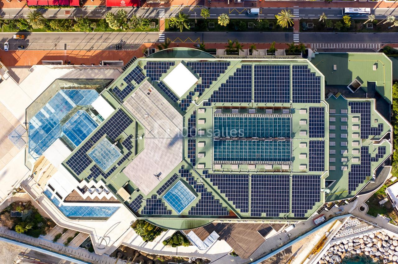 Vue aérienne d'un bâtiment avec des panneaux solaires sur le toit, entouré de routes et d'espaces urbains.