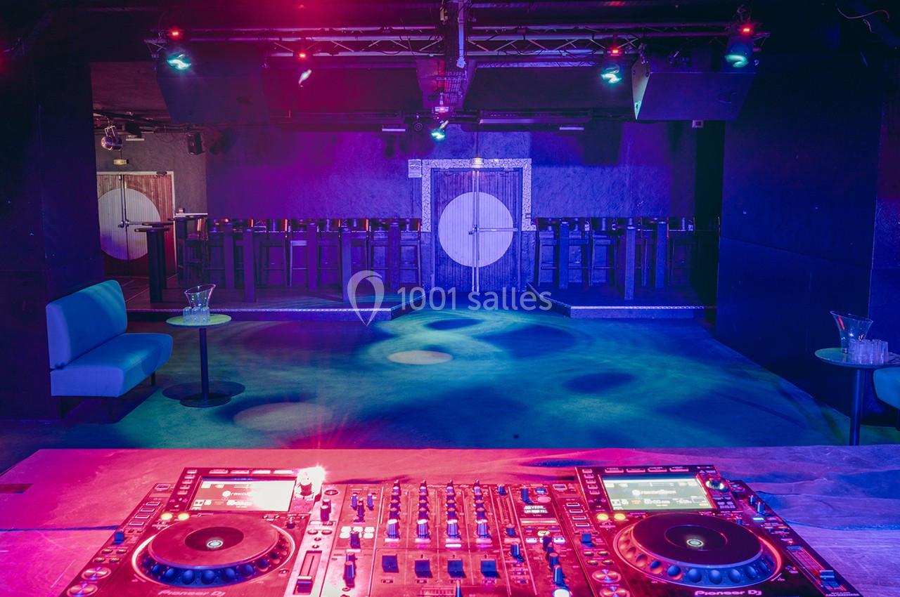 Salle de discothèque vide avec une console de DJ au premier plan, éclairée par des lumières colorées.