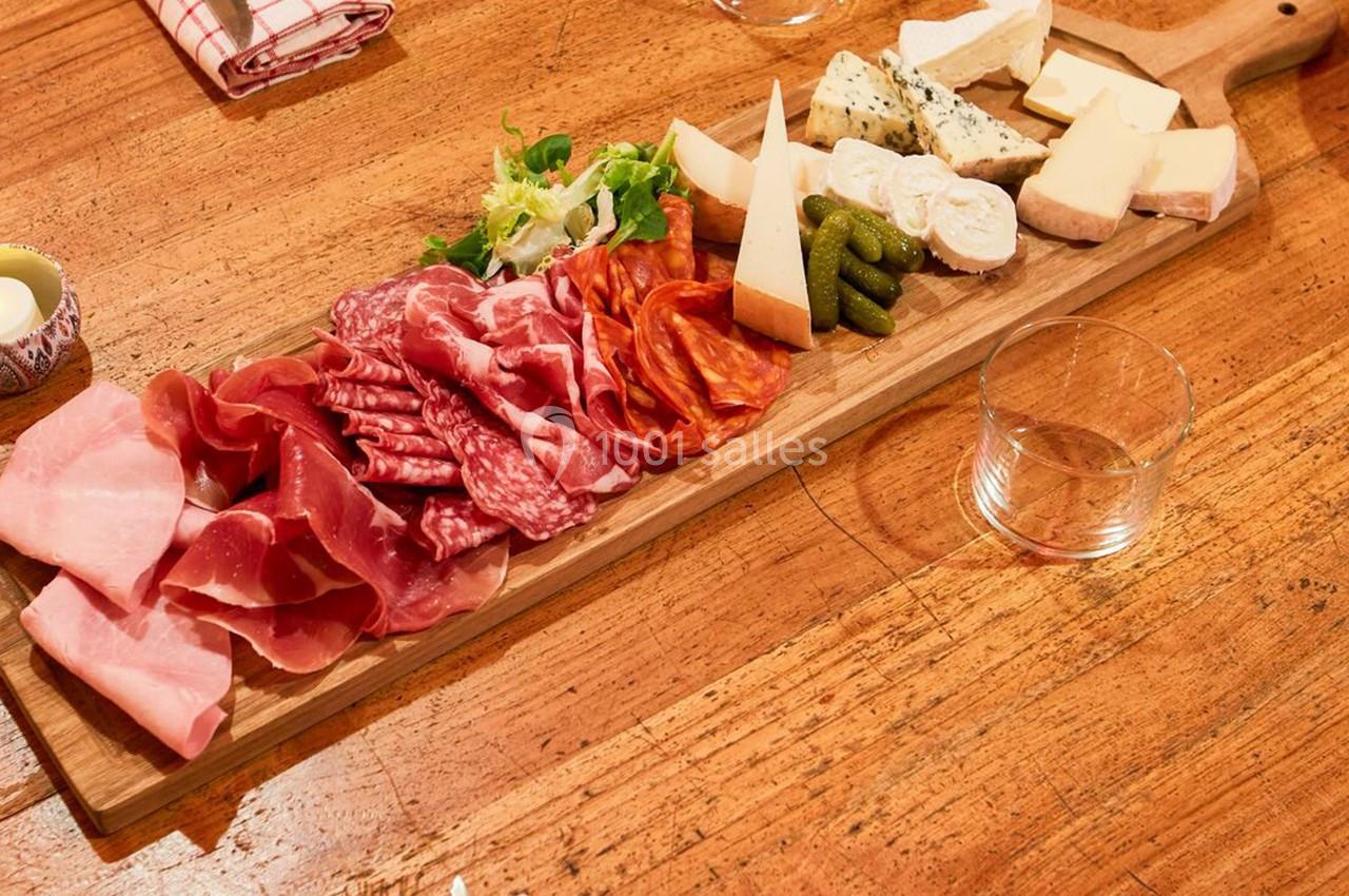 Plateau en bois garni de charcuteries, fromages, cornichons et salade, posé sur une table en bois.