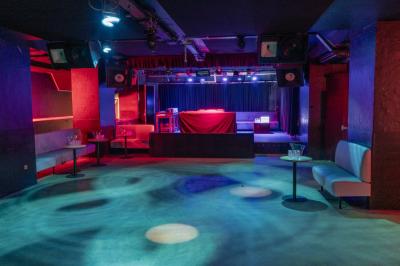 Salle sombre avec parquet, bar à droite, banquettes noires sur les côtés et éclairage tamisé.