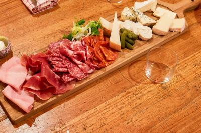 Plateau en bois garni de charcuteries, fromages, cornichons et salade, posé sur une table en bois.