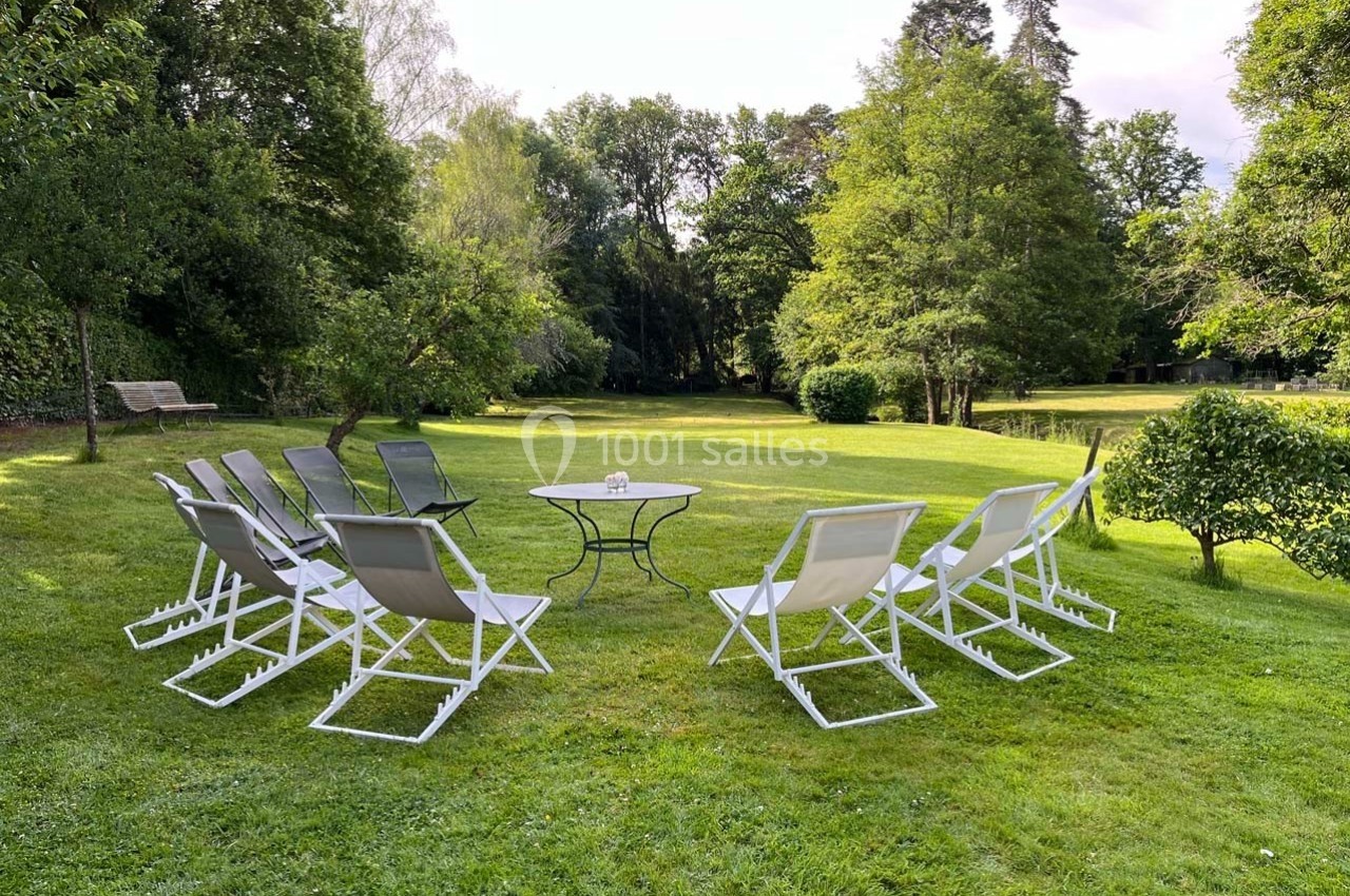 Chaises pliantes disposées en cercle autour d'une table basse sur une pelouse entourée d'arbres dans un jardin.