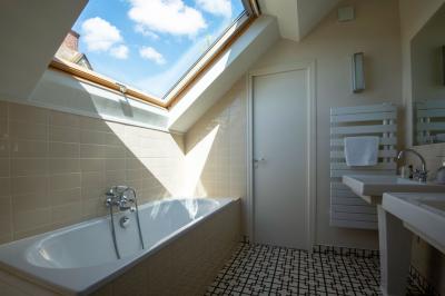 Table en bois clair avec un livre, une carte et un vase contenant une fleur verte, près d'un fauteuil blanc.