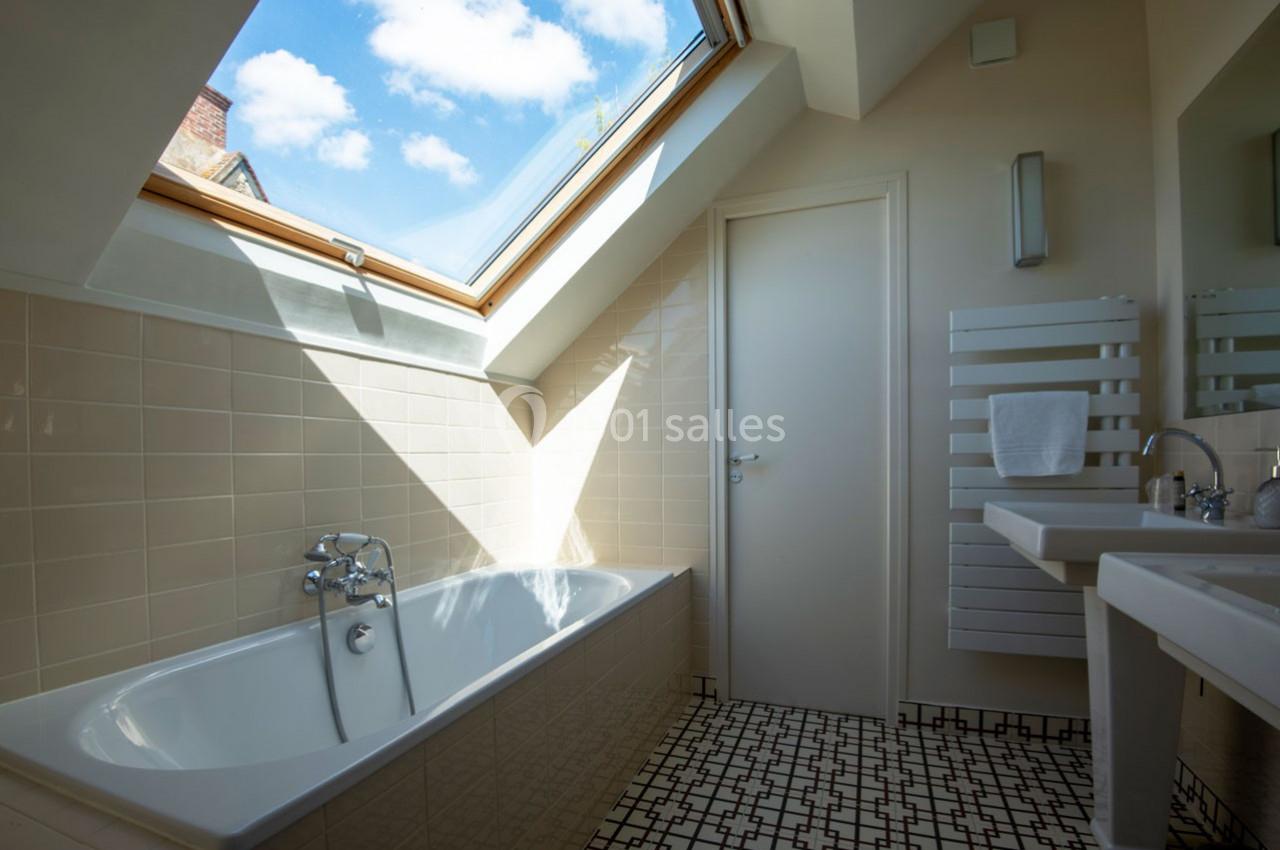 Salle de bain lumineuse avec baignoire, fenêtre de toit laissant entrer la lumière naturelle et carrelage géométrique au sol.