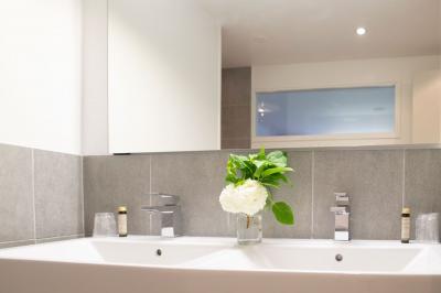 Table en bois clair avec un livre, une carte et un vase contenant une fleur verte, près d'un fauteuil blanc.