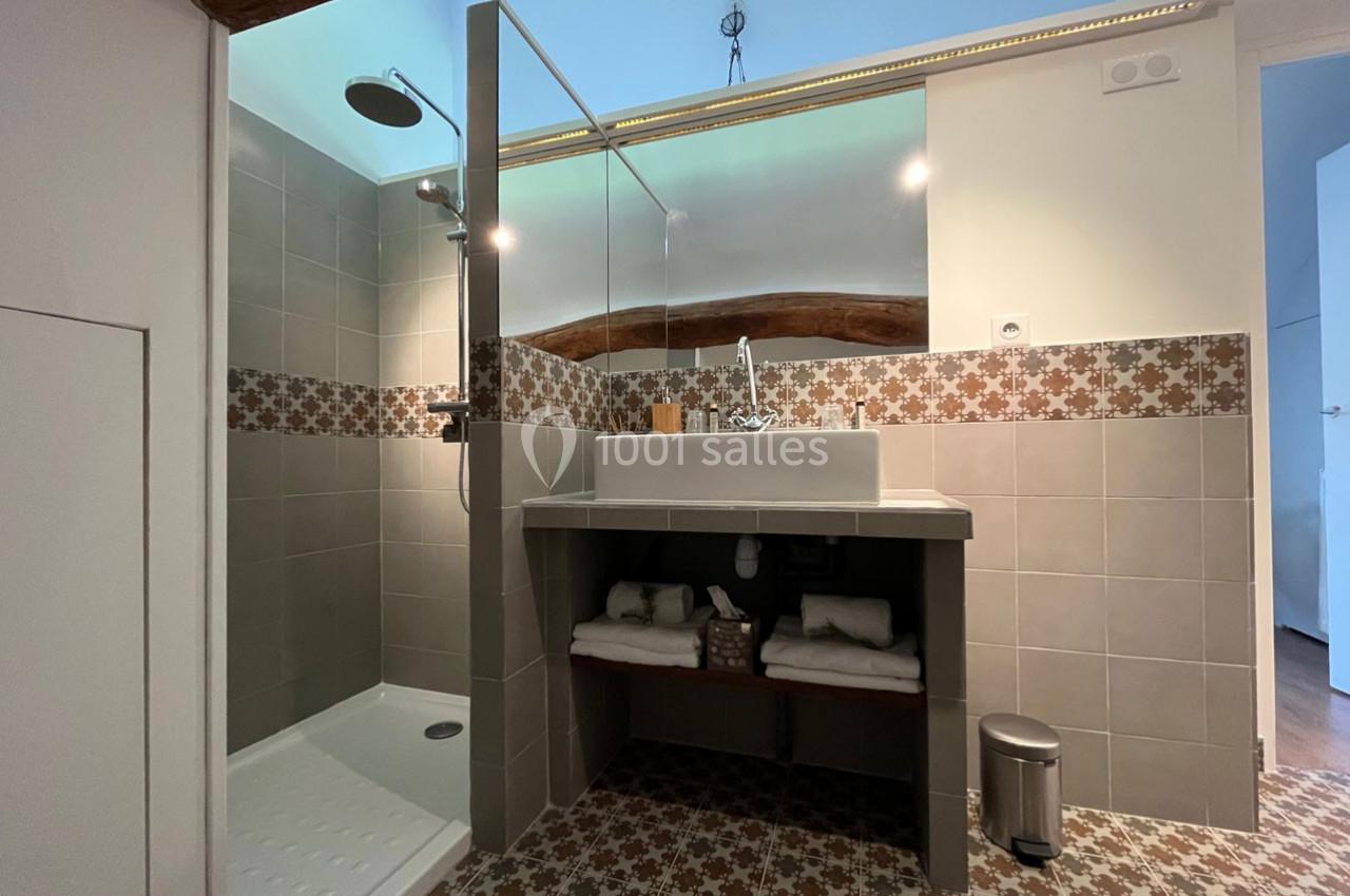 Salle de bain avec douche à l'italienne, lavabo sur meuble en bois, miroir et carrelage à motifs géométriques.