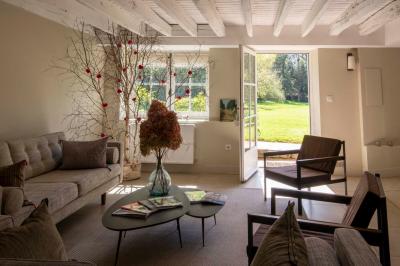 Table en bois clair avec un livre, une carte et un vase contenant une fleur verte, près d'un fauteuil blanc.