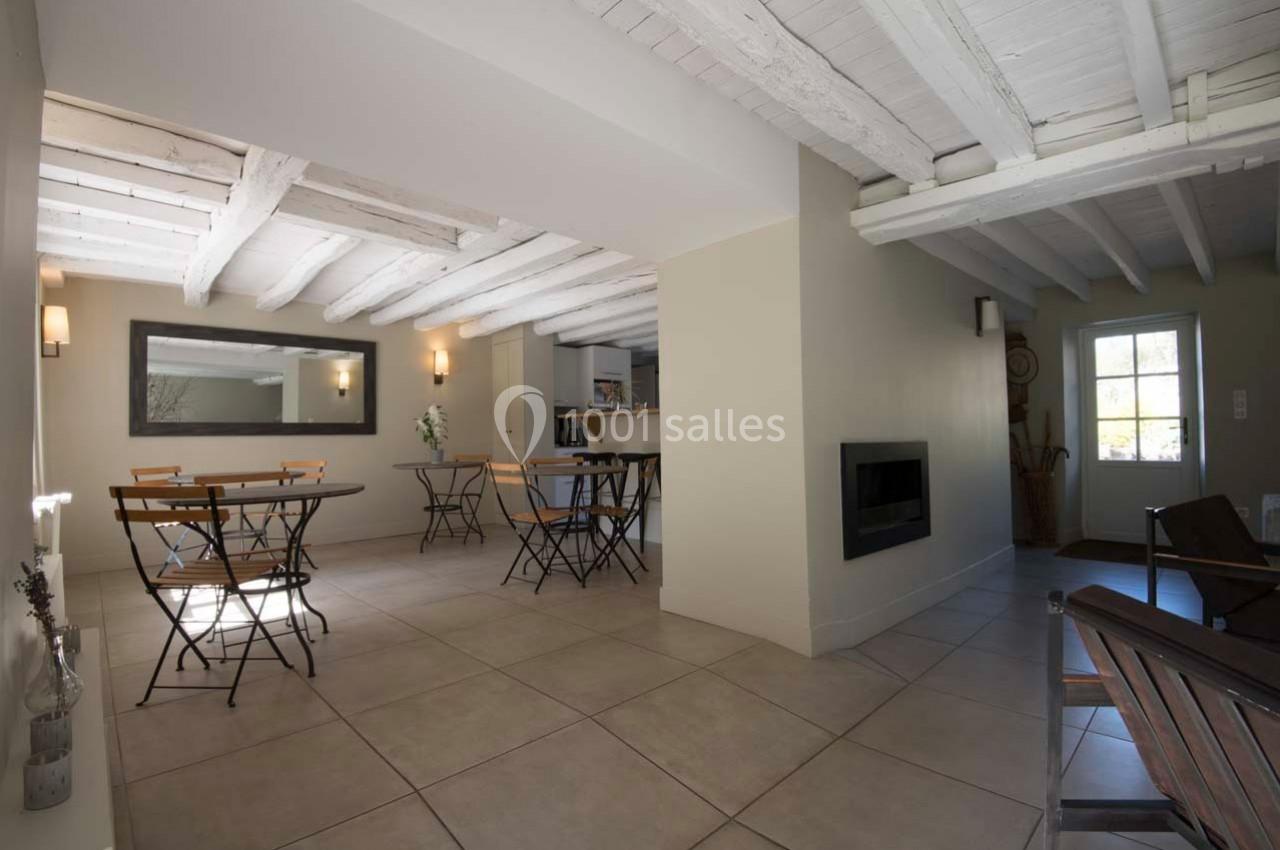 Salle lumineuse avec tables et chaises en métal, plafond en poutres blanches et porte vitrée donnant sur l'extérieur.