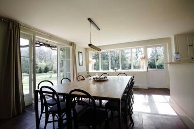 Table en bois clair avec un livre, une carte et un vase contenant une fleur verte, près d'un fauteuil blanc.