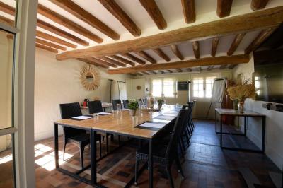Table en bois clair avec un livre, une carte et un vase contenant une fleur verte, près d'un fauteuil blanc.