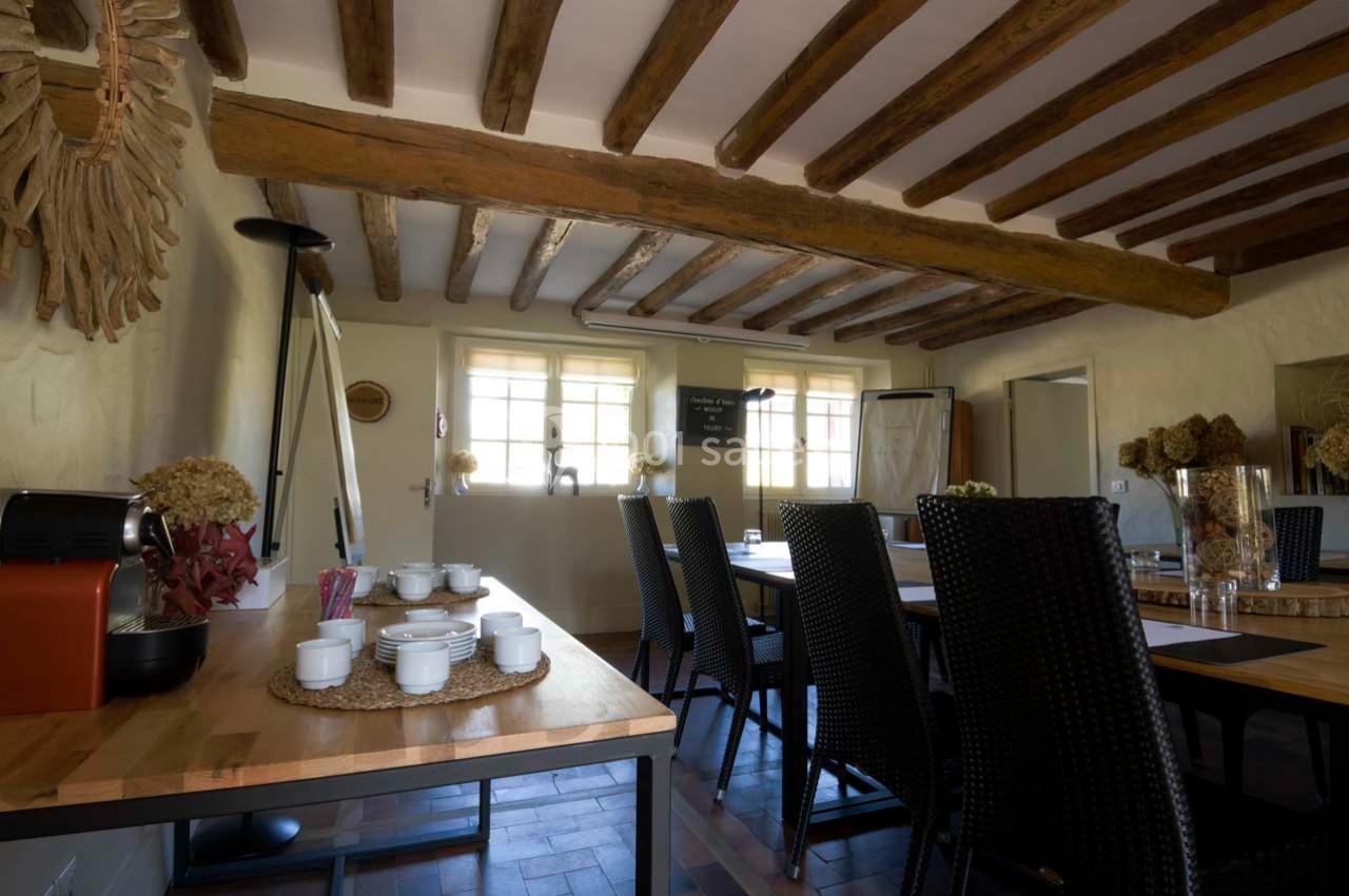 Salle de réunion lumineuse avec poutres apparentes, table en bois, chaises en osier et matériel de présentation.