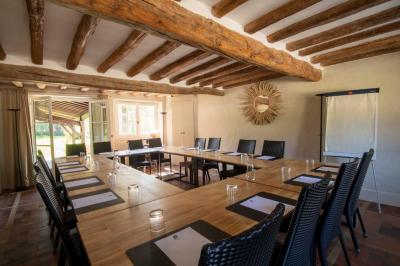 Table en bois clair avec un livre, une carte et un vase contenant une fleur verte, près d'un fauteuil blanc.