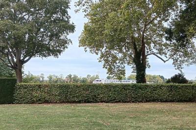 Façade d'une grande maison en pierre claire avec volets bleus, entourée d'un jardin et d'une allée gravillonnée.