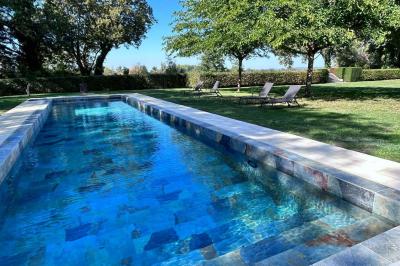 Façade d'une grande maison en pierre claire avec volets bleus, entourée d'un jardin et d'une allée gravillonnée.