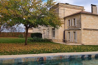 Façade d'une grande maison en pierre claire avec volets bleus, entourée d'un jardin et d'une allée gravillonnée.