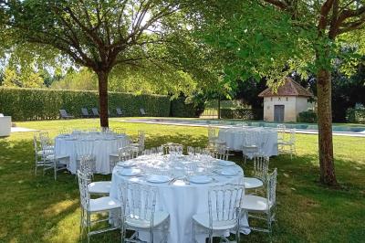 Façade d'une grande maison en pierre claire avec volets bleus, entourée d'un jardin et d'une allée gravillonnée.