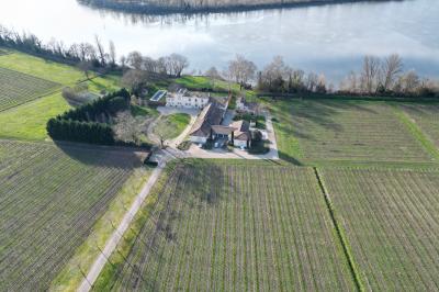 Façade d'une grande maison en pierre claire avec volets bleus, entourée d'un jardin et d'une allée gravillonnée.