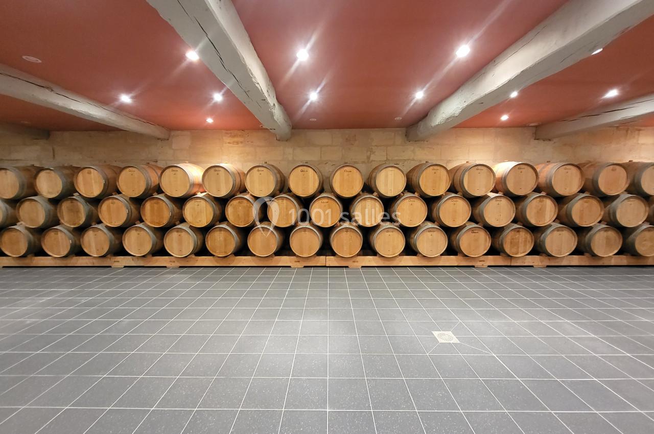 Rangées de tonneaux en bois alignés dans une cave avec un sol carrelé et un plafond éclairé.