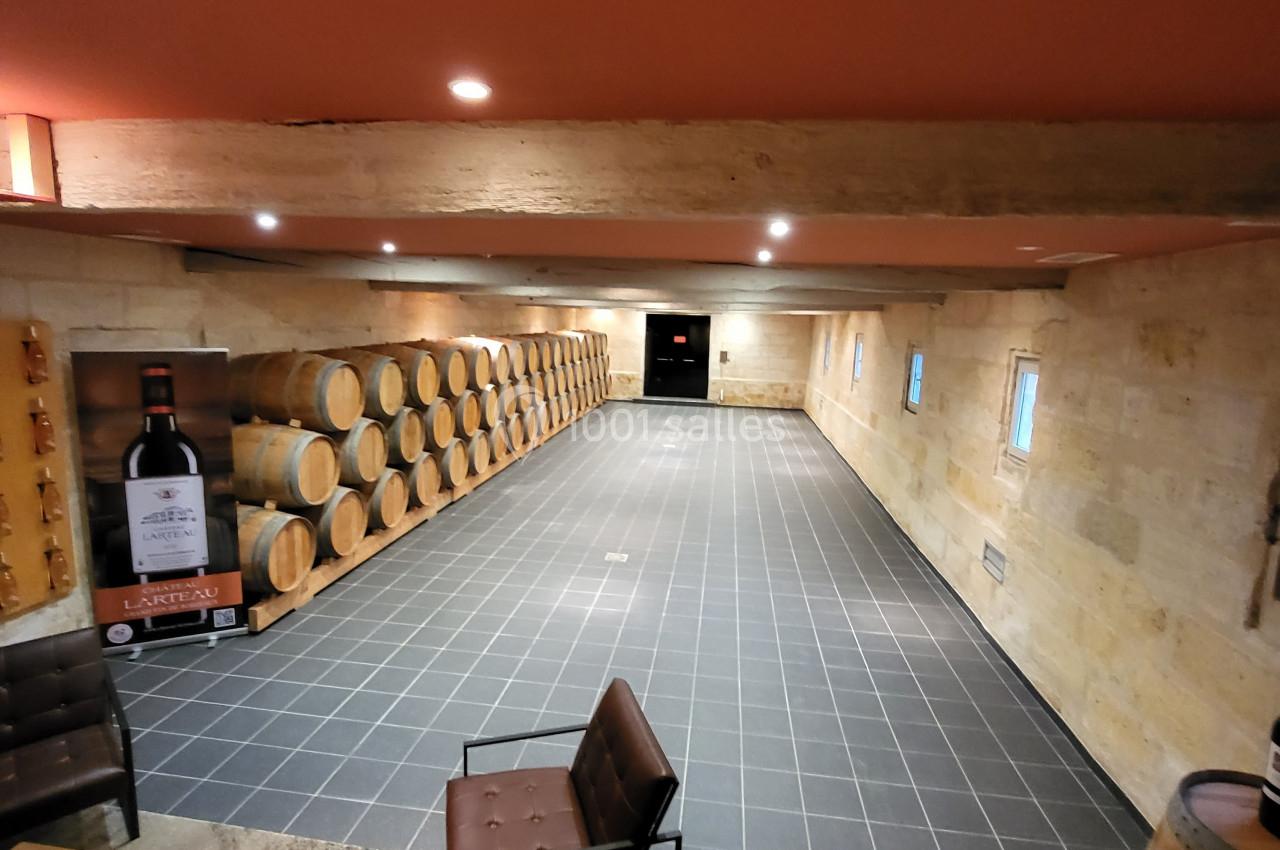 Salle de dégustation avec barriques en bois alignées le long d'un mur en pierre et mobilier moderne au premier plan.