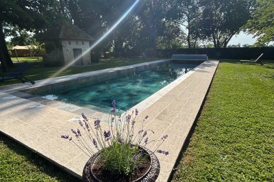 Façade d'une grande maison en pierre claire avec volets bleus, entourée d'un jardin et d'une allée gravillonnée.