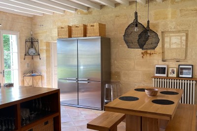 Façade d'une grande maison en pierre claire avec volets bleus, entourée d'un jardin et d'une allée gravillonnée.