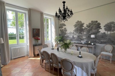 Façade d'une grande maison en pierre claire avec volets bleus, entourée d'un jardin et d'une allée gravillonnée.