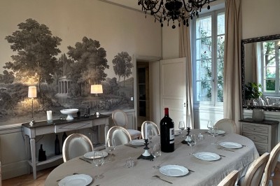 Façade d'une grande maison en pierre claire avec volets bleus, entourée d'un jardin et d'une allée gravillonnée.