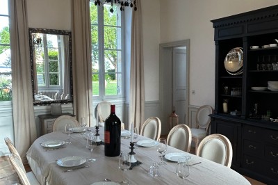 Façade d'une grande maison en pierre claire avec volets bleus, entourée d'un jardin et d'une allée gravillonnée.