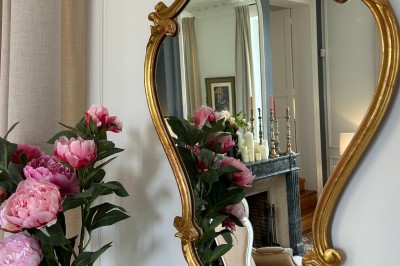 Façade d'une grande maison en pierre claire avec volets bleus, entourée d'un jardin et d'une allée gravillonnée.