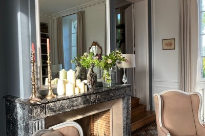 Façade d'une grande maison en pierre claire avec volets bleus, entourée d'un jardin et d'une allée gravillonnée.