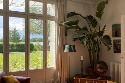 Façade d'une grande maison en pierre claire avec volets bleus, entourée d'un jardin et d'une allée gravillonnée.