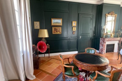 Façade d'une grande maison en pierre claire avec volets bleus, entourée d'un jardin et d'une allée gravillonnée.