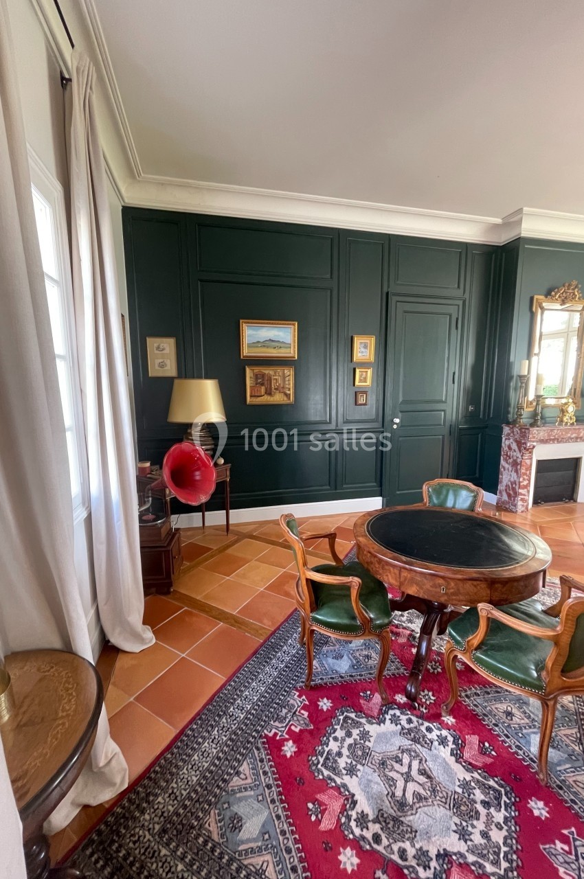 Salle de séjour élégante avec murs verts, table ronde en bois, gramophone rouge et cheminée ornée d'un miroir.