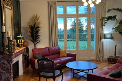 Façade d'une grande maison en pierre claire avec volets bleus, entourée d'un jardin et d'une allée gravillonnée.